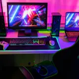 Gamingowy zestaw z podświetlaną klawiaturą i myszką, kontrolerem, głośnikami i laptopem. Kolorowe światła tworzą atmosferę, jakby komputer sam się wyłączał.