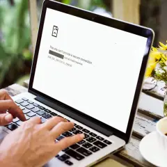 Osoba pisze na laptopie, na ekranie błąd ERR_SSL_PROTOCOL_ERROR. Obok kawa i kwiaty.