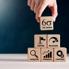 Dłoń układa kostkę z symbolem Six Sigma na piramidzie z kostek: Define, Measure, Analyze, Improve, Control.