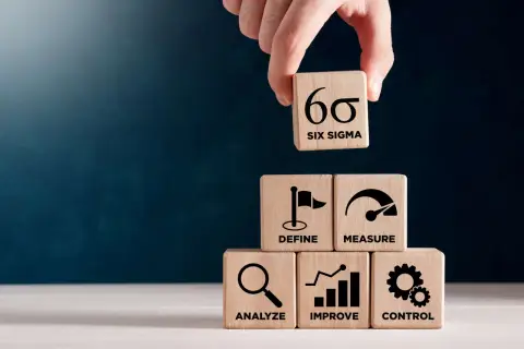 Dłoń układa kostkę z symbolem Six Sigma na piramidzie z kostek: Define, Measure, Analyze, Improve, Control.