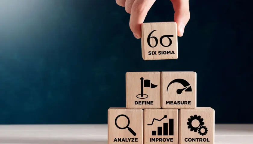 Dłoń układa kostkę z symbolem Six Sigma na piramidzie z kostek: Define, Measure, Analyze, Improve, Control.